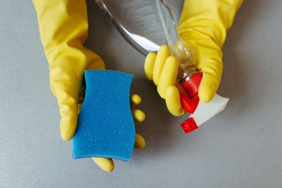 Hands wearing yellow gloves holding a sponge and a spray bottle.
